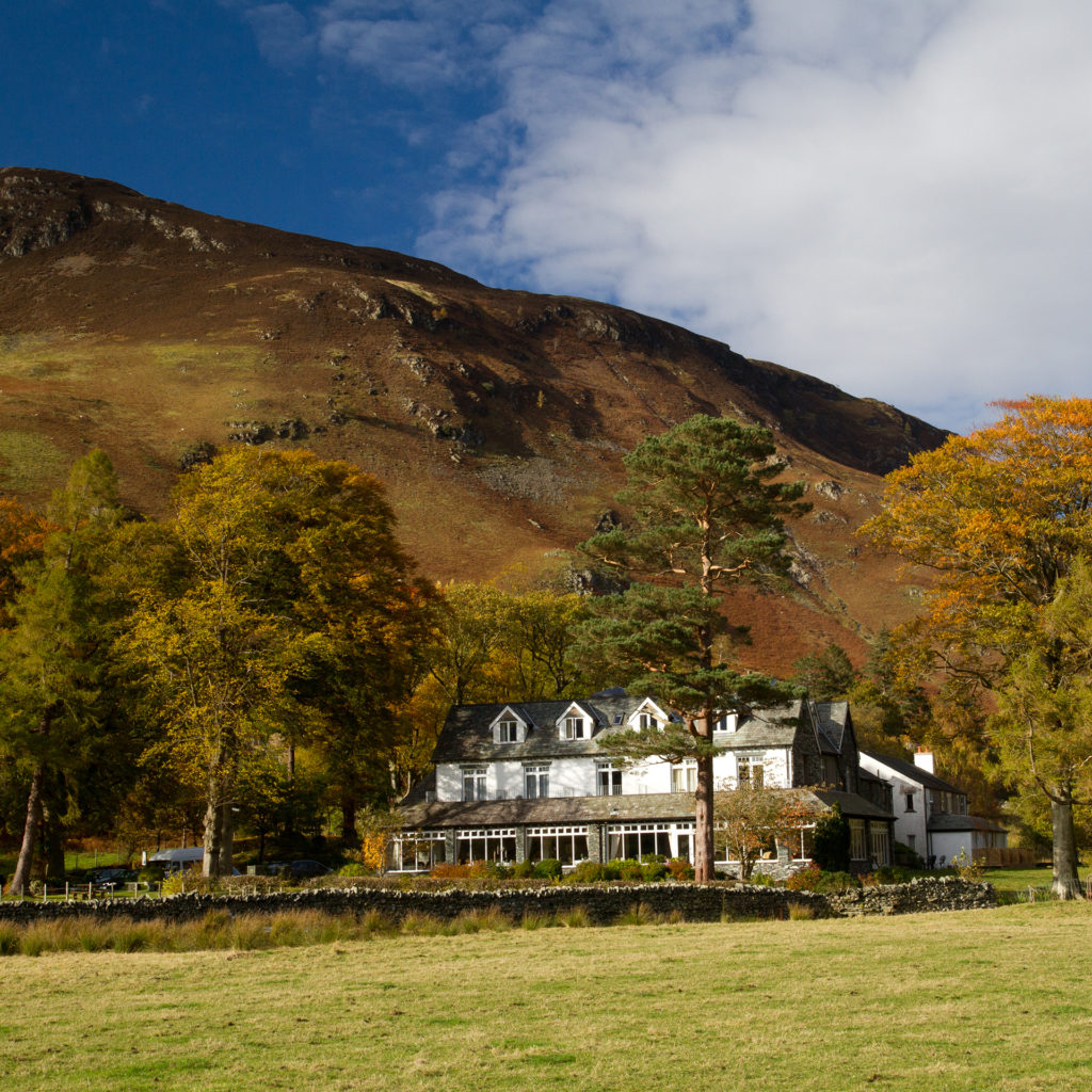 White painted, grey roofed hotel seen across field, autumn trees around, mountain behind