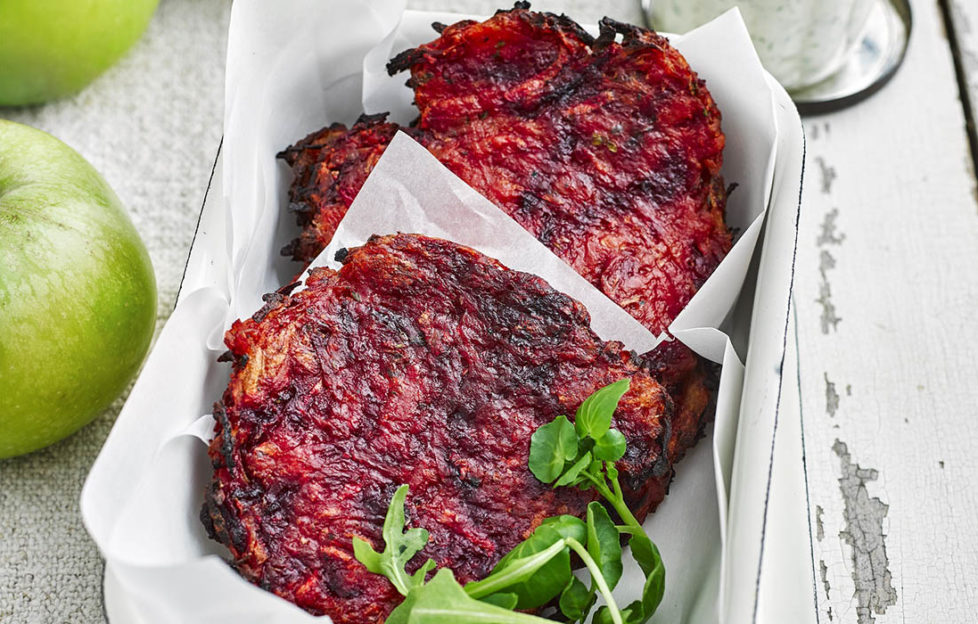 Two beetroot-coloured potato cakes in a dish with greaseproof paper, Bramley apples and dill yogurt on the side