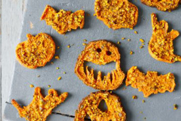 Tray of orange crispy sweet potato and pumpkin seed chews cut into bat and scary face shapes