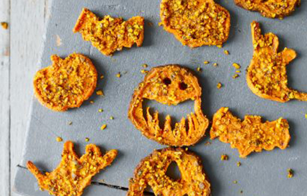 Tray of orange crispy sweet potato and pumpkin seed chews cut into bat and scary face shapes