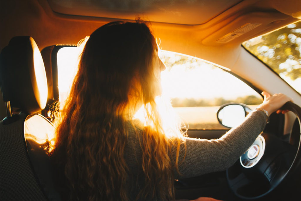 Side view of long-haired woman driving, golden sunshine behind her, 