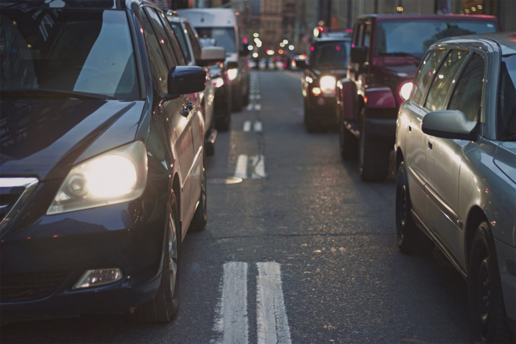 Two lanes of cars in city centre traffic jam, twilight, headlights on