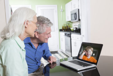 A senior couple use a laptop computer at home to video-chat with their grandson.