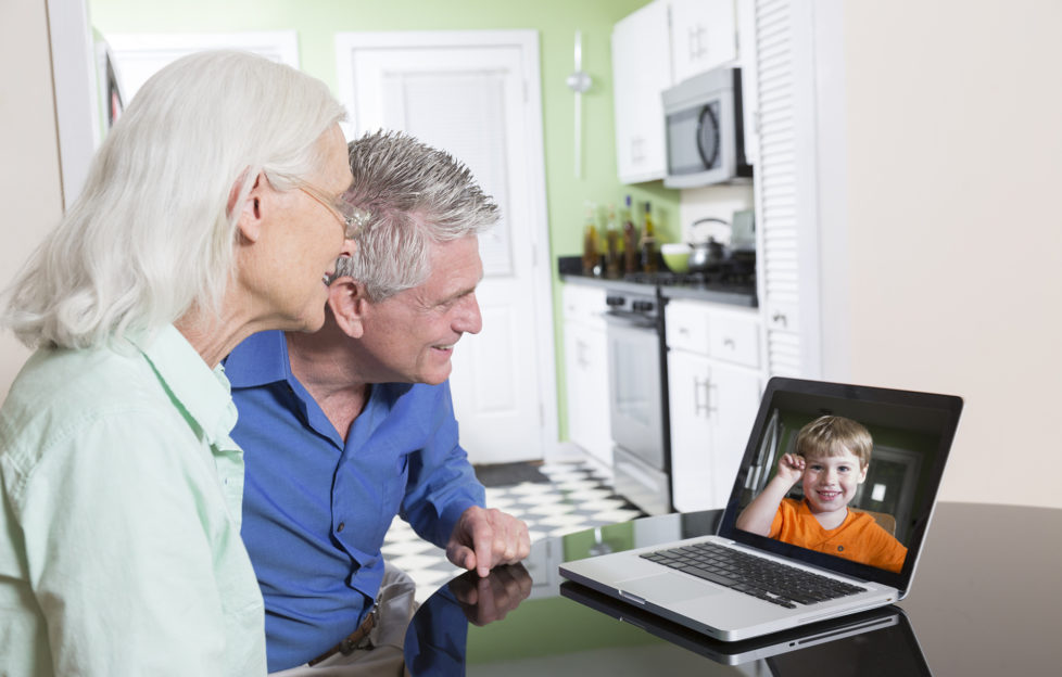 A senior couple use a laptop computer at home to video-chat with their grandson.