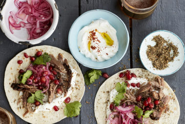 lamb tacos ready to roll up, colourful with red onion and pomegranate seeds, yogurt in a blue dish