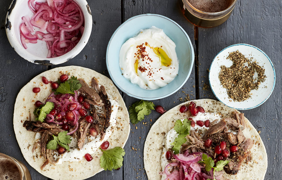 lamb tacos ready to roll up, colourful with red onion and pomegranate seeds, yogurt in a blue dish