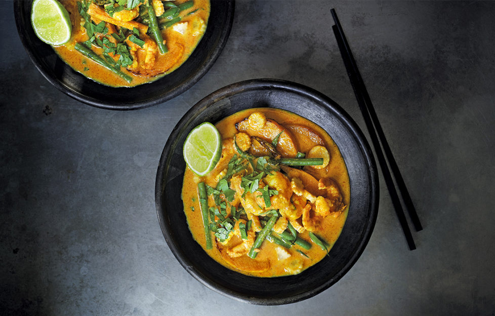 yellow thai curry in 2 black bowls, chopsticks on side, golden curry with green beans, fresh coriander and slice of lime