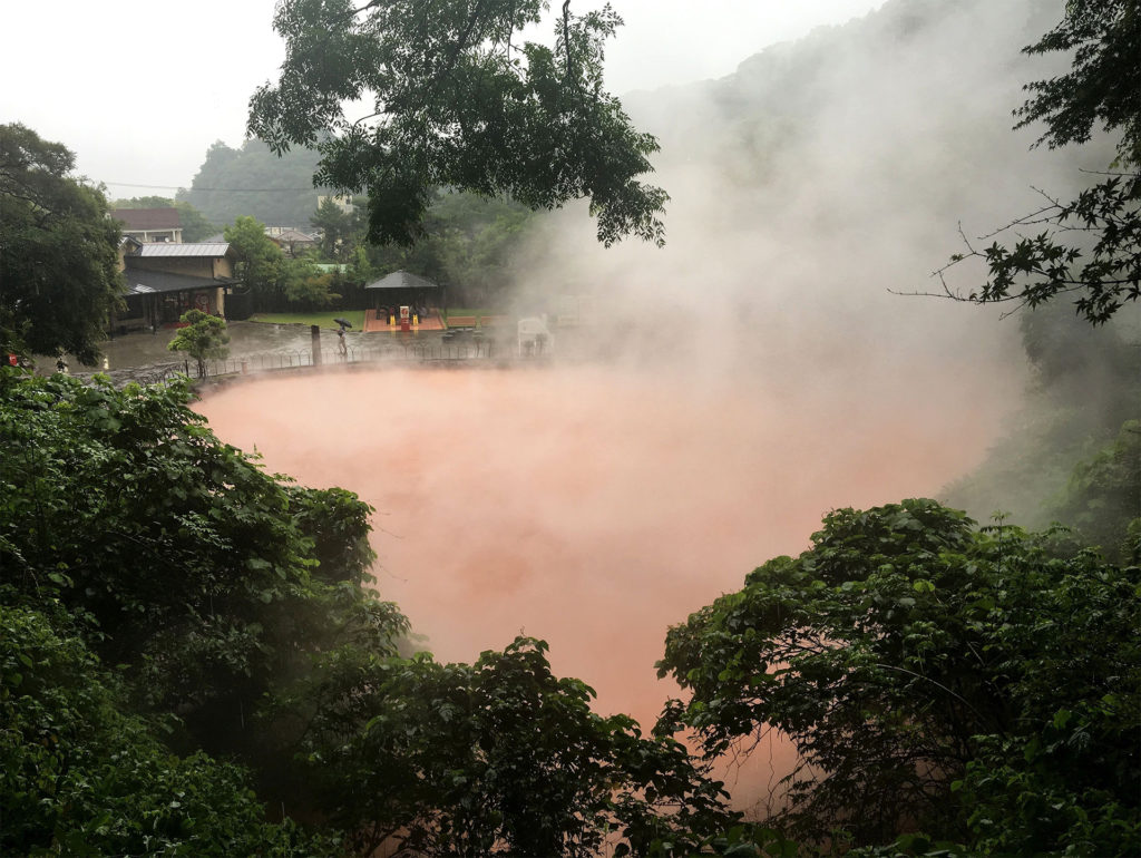 Reddish-brown steaming water seen through lush vegetation