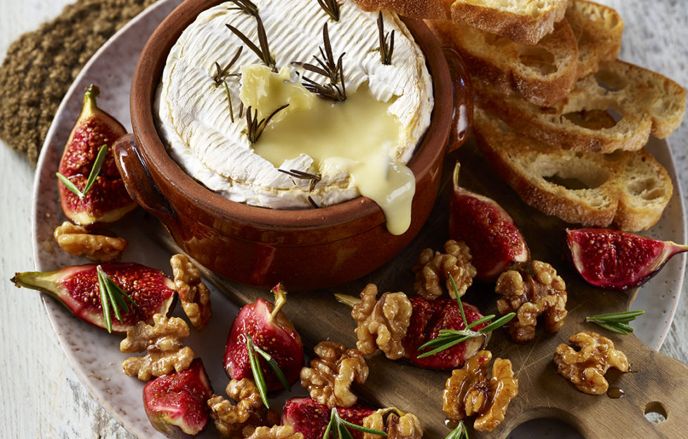 Melted Camembert cheese in dish, walnut halves, quartered fresh figs and rosemary sprigs