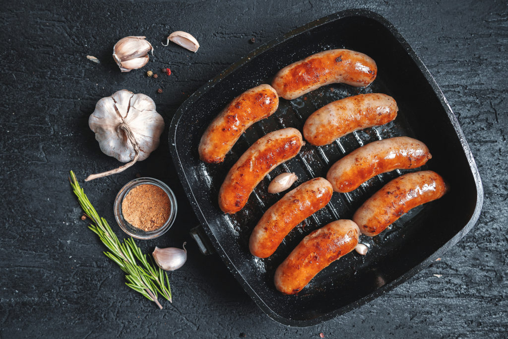 Top view on fried sausages in a black frying pan on a black stone table