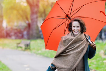 Older woman walking in the park with an orange umbrella