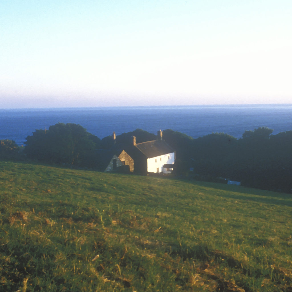 View over hillside to deep blue sea of Cardigan Bay, white painted farmhouse visible among trees
