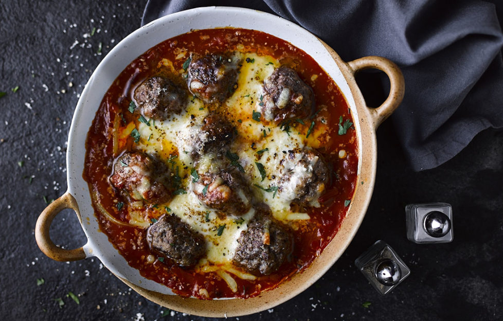 Cast iron casserole dish with baked meatballs in tomato sauce, covered in melted chees