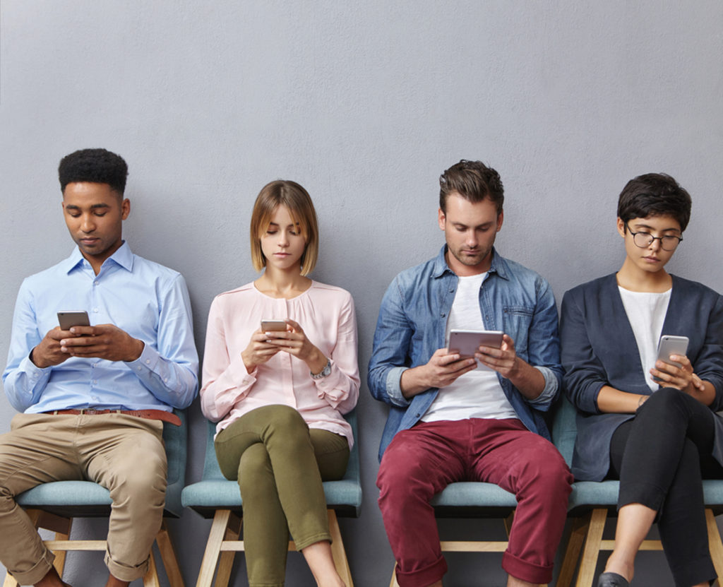 4 people all sitting and looking at their phones