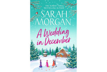 Cover of A Wedding In December. A couple and two women in wedding outfits are following a path through the snow to a log cabin. Large pine trees are decorated with lights.