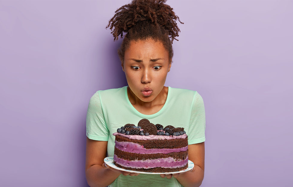 Woman looks longingly at gorgeous looking chocolate and cream cake topped with oreo biscuits and blackberries
