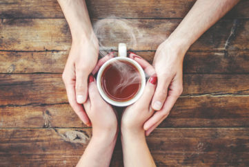 A cup of tea in the hands of a man and a woman.