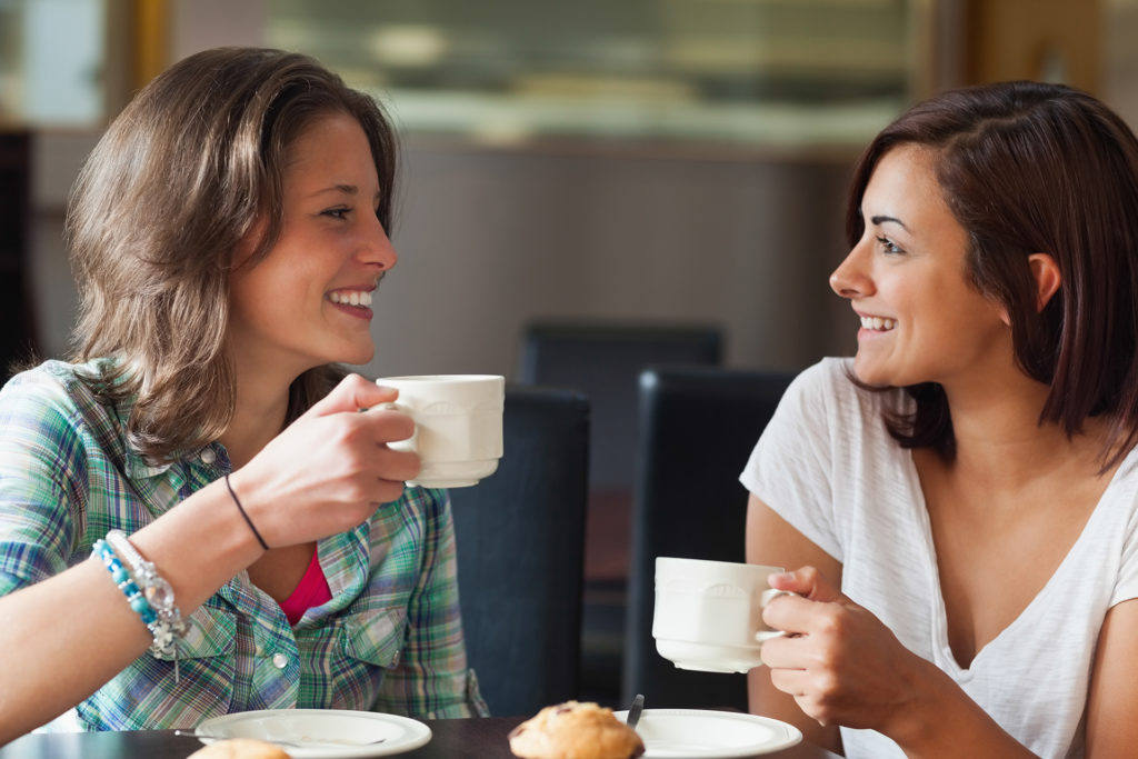 Two smiling students having a cup of coffee in college canteen for health benefits kindness
