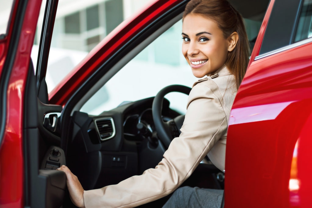 smiling woman opening door of her red car