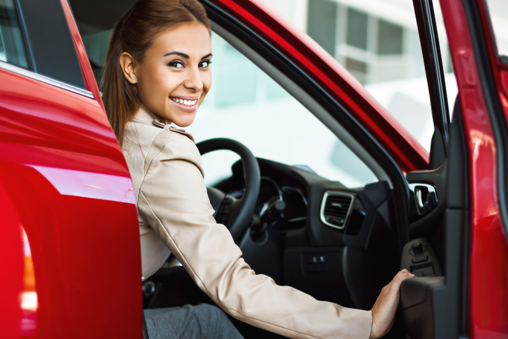 smiling woman opening door of her red car