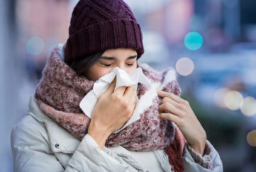 Pretty young woman blowing her nose with a tissue outdoor in winter. Young woman getting sick with flu in a winter day. Woman with a cold.;
