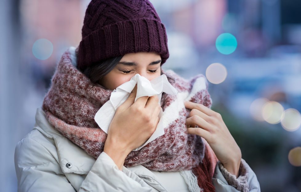 Pretty young woman blowing her nose with a tissue outdoor in winter. Young woman getting sick with flu in a winter day. Woman with a cold.;