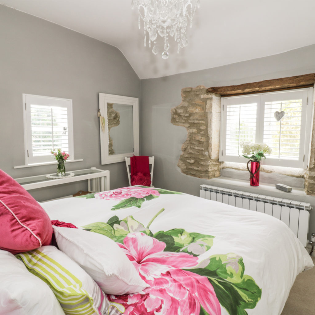Cottage bedroom, huge bright pink flowers on bedlinen, original beam and stonework visible around window