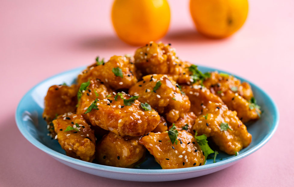 Shallow dish of chicken pieces coated in crispy golden batter and orange sauce,, sesame seeds and sprinkled with coriander