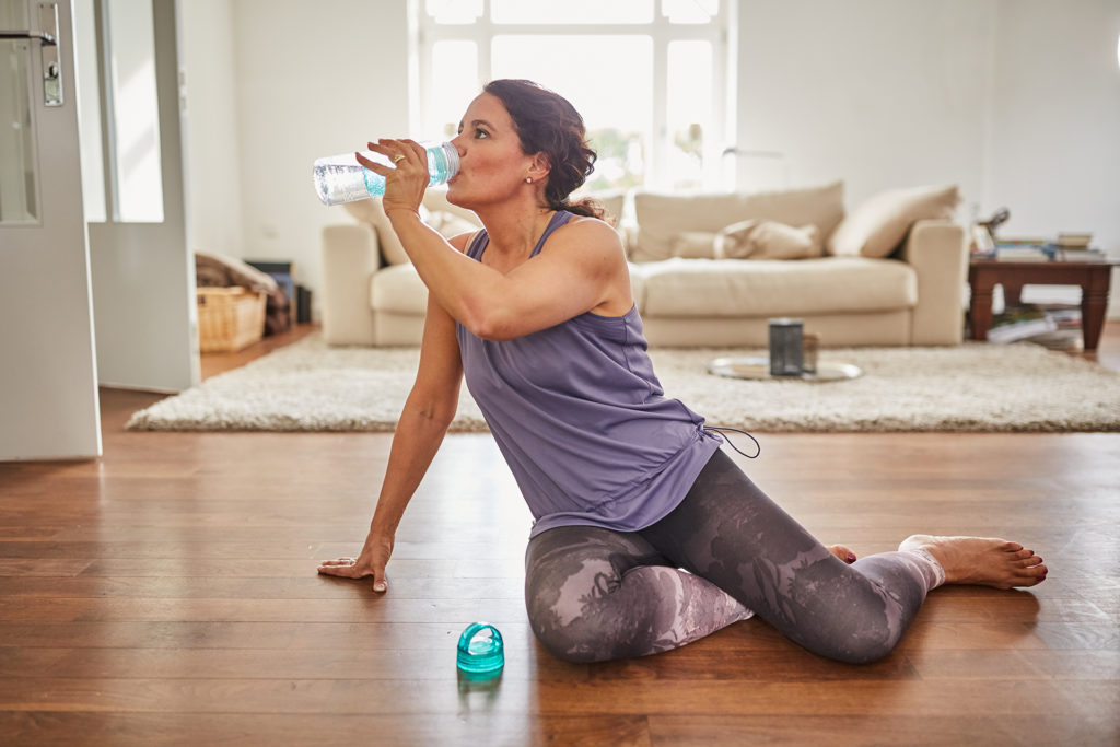 Woman drinking water and exercising in her front room
