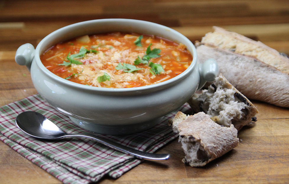 Blue earthenware soup bowl on rustic table, filled with rich orange minestrone soup liberally sprinkled with parmesan cheese