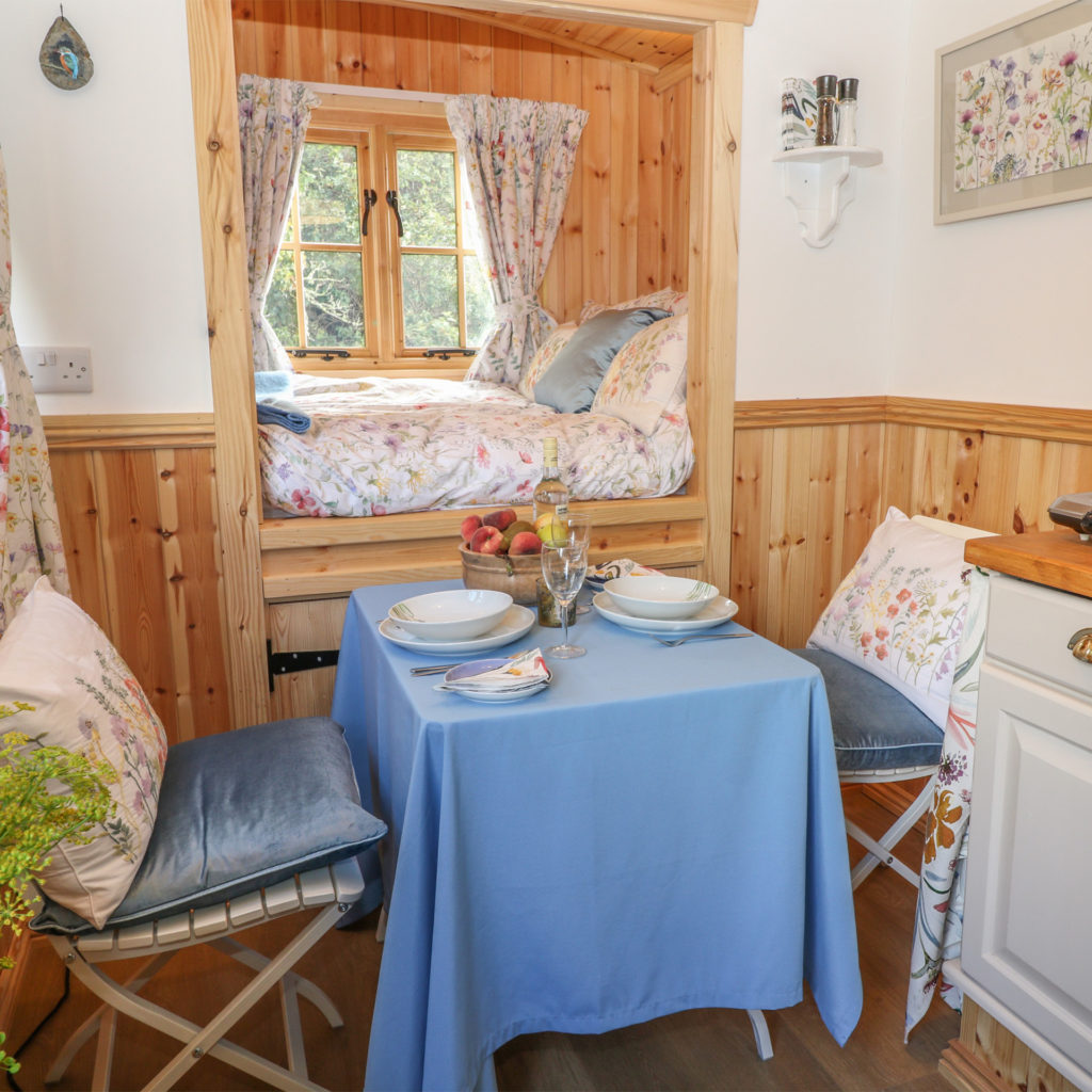 Corner of kitchen unit, tiny table for 2, and truckle bed set into wood panelled wall and window, view over countryside