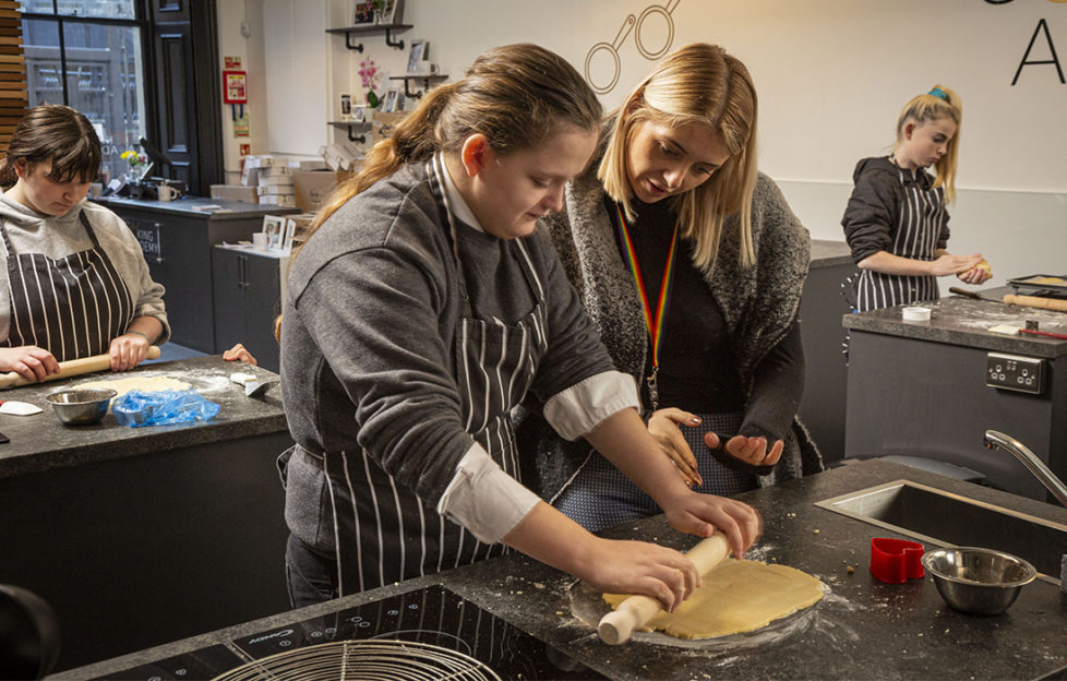 Three young people in cook's aprons working at kitchen work stations