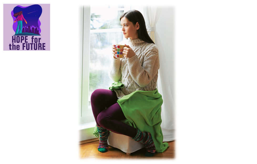 Young woman in thick purple tights sitting on pouffe looking out of the window, holding a mug, looking sad and tense