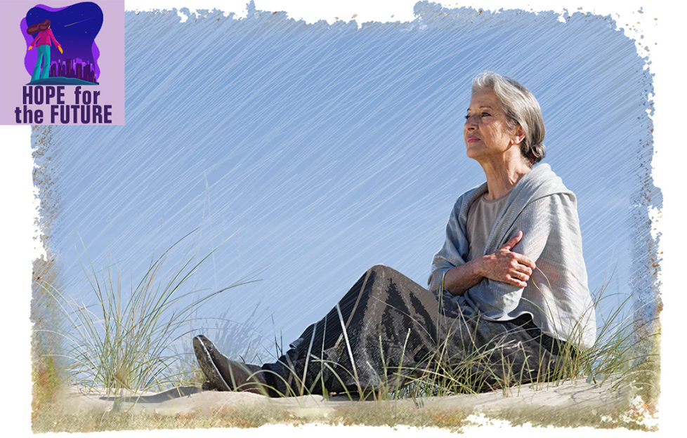 Mature woman sitting on sand dune, looking out to sea, sea grass in foreground