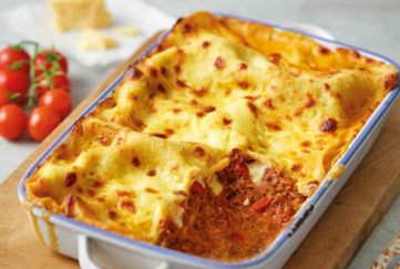 Ovenproof dish filled with golden brown cheese-topped lasagne, one portion scooped out revealing tomatoey mixture
