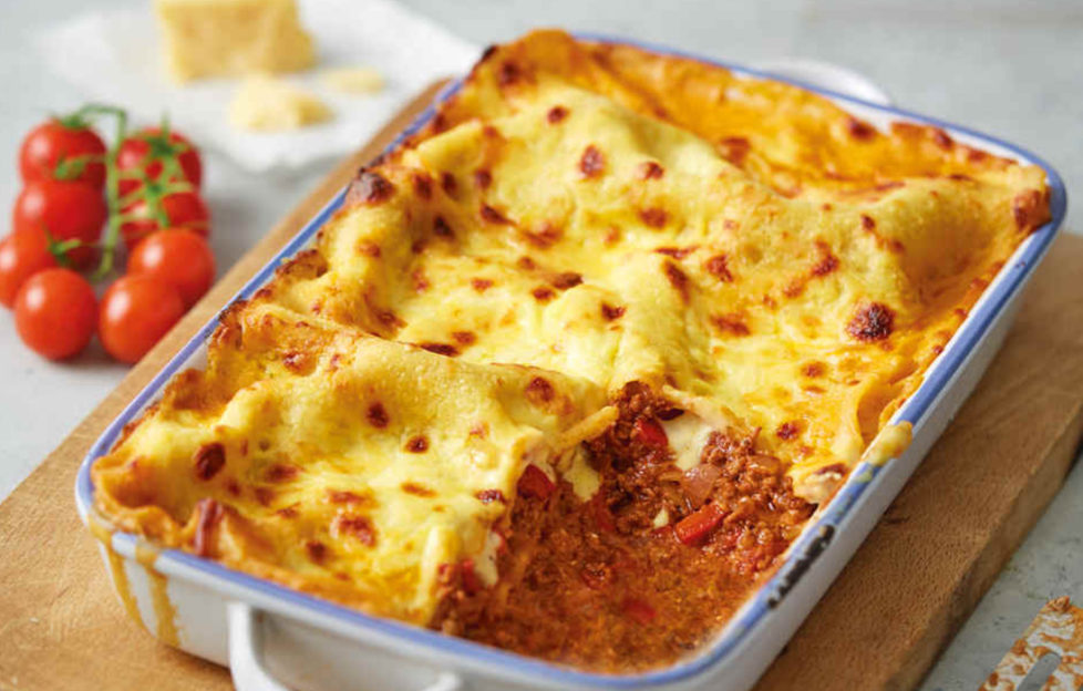 Ovenproof dish filled with golden brown cheese-topped lasagne, one portion scooped out revealing tomatoey mixture