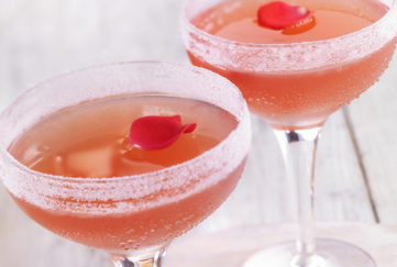 Two sugar-rimmed wide champagne glasses rose wine mocktail, garnished with rose petals