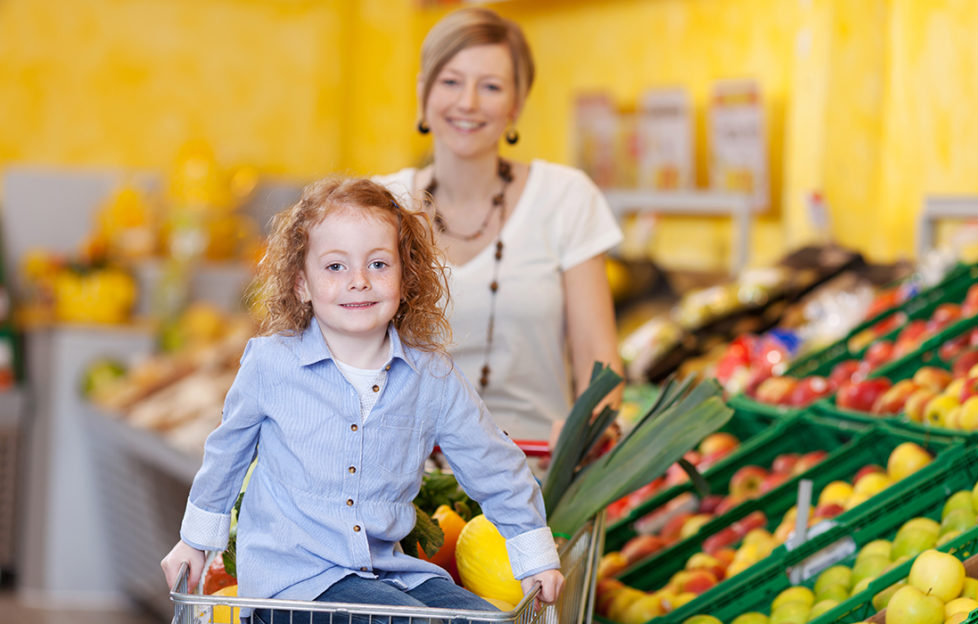 mother in a supermarket pushing a trolley filled with fresh fruit and veg with the daughter riding on the front