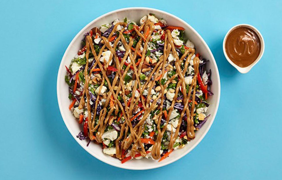 Bowl of cauliflower rice salad with zig zag drizzle of peanut dressing across the top