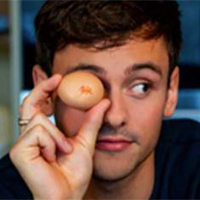 Diver Tom Daley poses, holding an egg up in front of one eye
