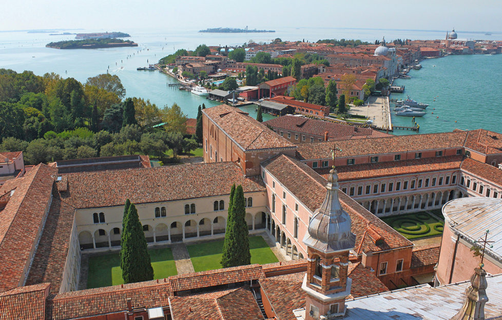 Venice: Pink brick quadrangles with manicured lawns, seen from tower, also turquoise water and an island with similar buildings in the middle distance