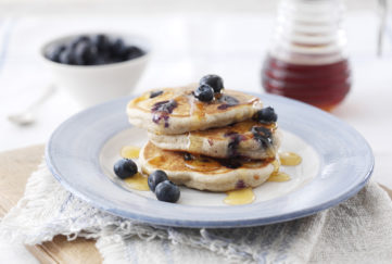 Stack of 3 small thick golden pancakes served with blueberries and syrup