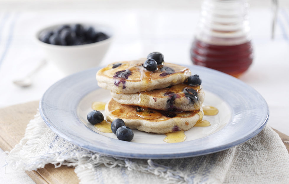 Stack of 3 small thick golden pancakes served with blueberries and syrup