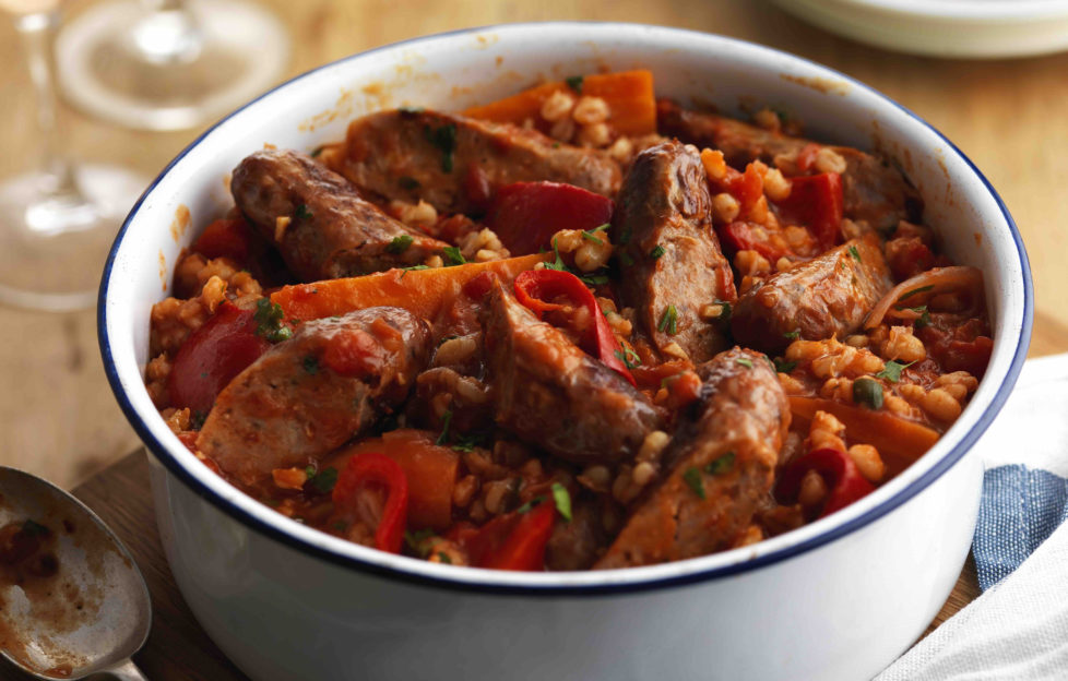 Round white casserole dish filled with mixture of sausage, barley, tomatoes and peppers