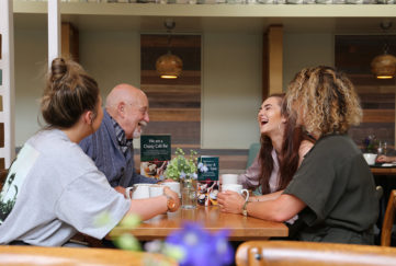 Three young people and an older man laughing together at a cafe table