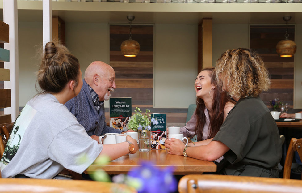 Three young people and an older man laughing together at a cafe table