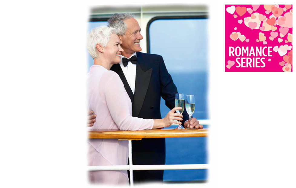 Mature couple in evening dress with glasses of sparkling wine lean on rail of cruise ship deck