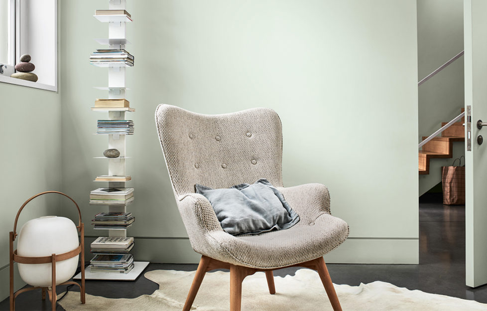 Comfy curved modern chair in front of pale green wall and tall, narrow modern shelf