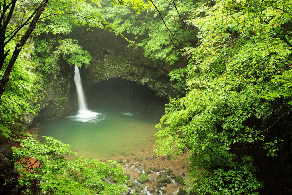 Small waterfall, green pool, ancient stone bridge and lush forest greenery
