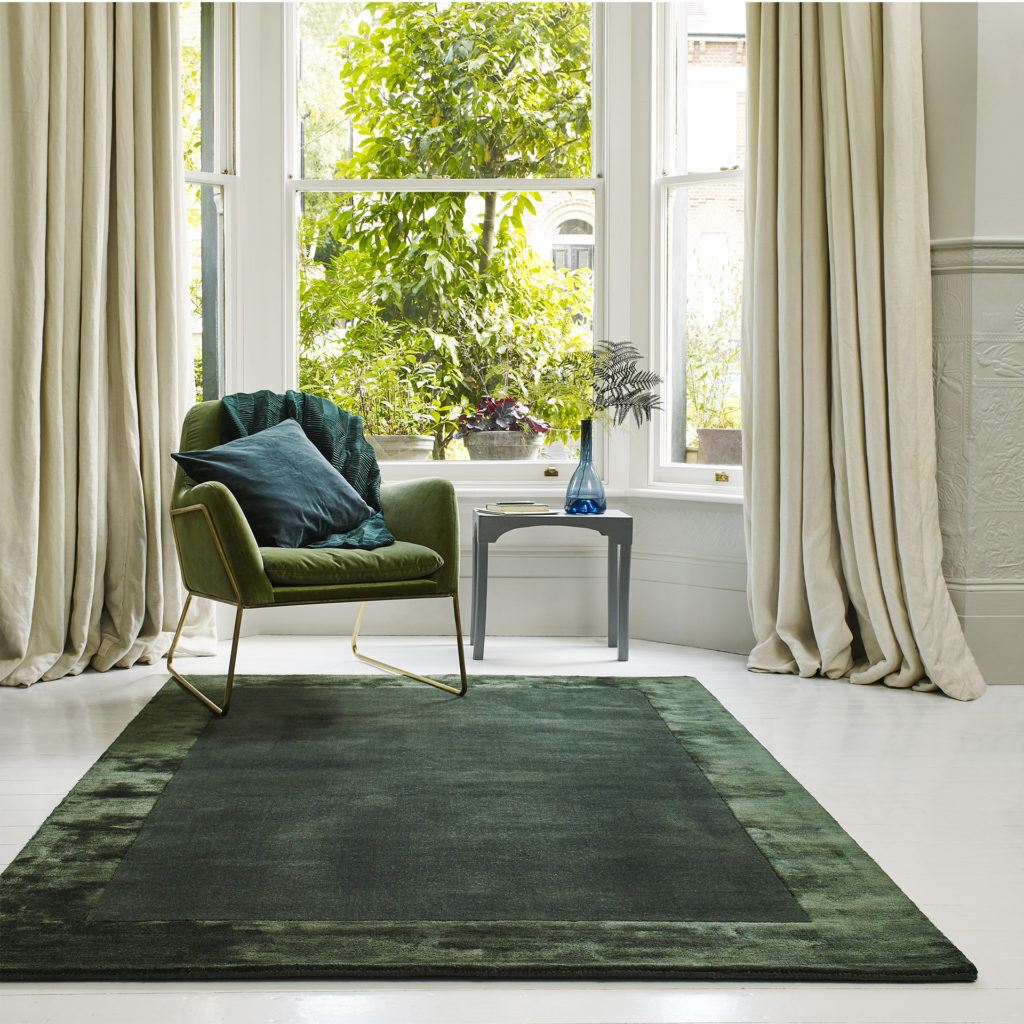 Victorian bay window, leafy shrub outside, cream curtains, modern forest green chair and large, rich, velvety forest green rug